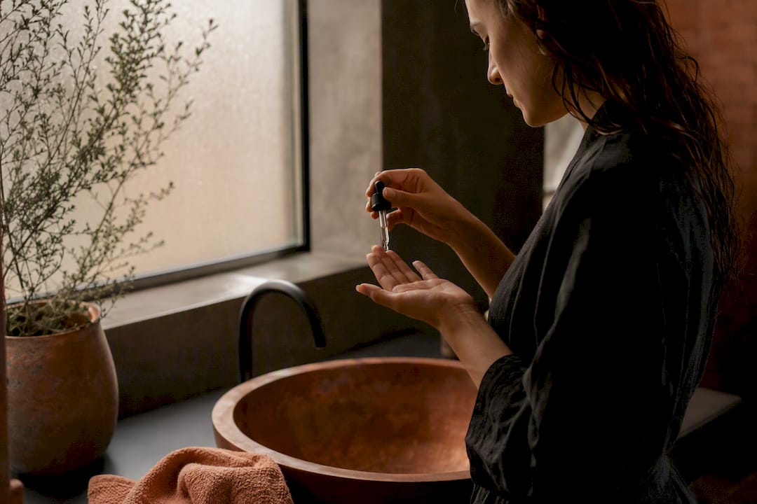 Hands applying copper peptide serum over ceramic dish